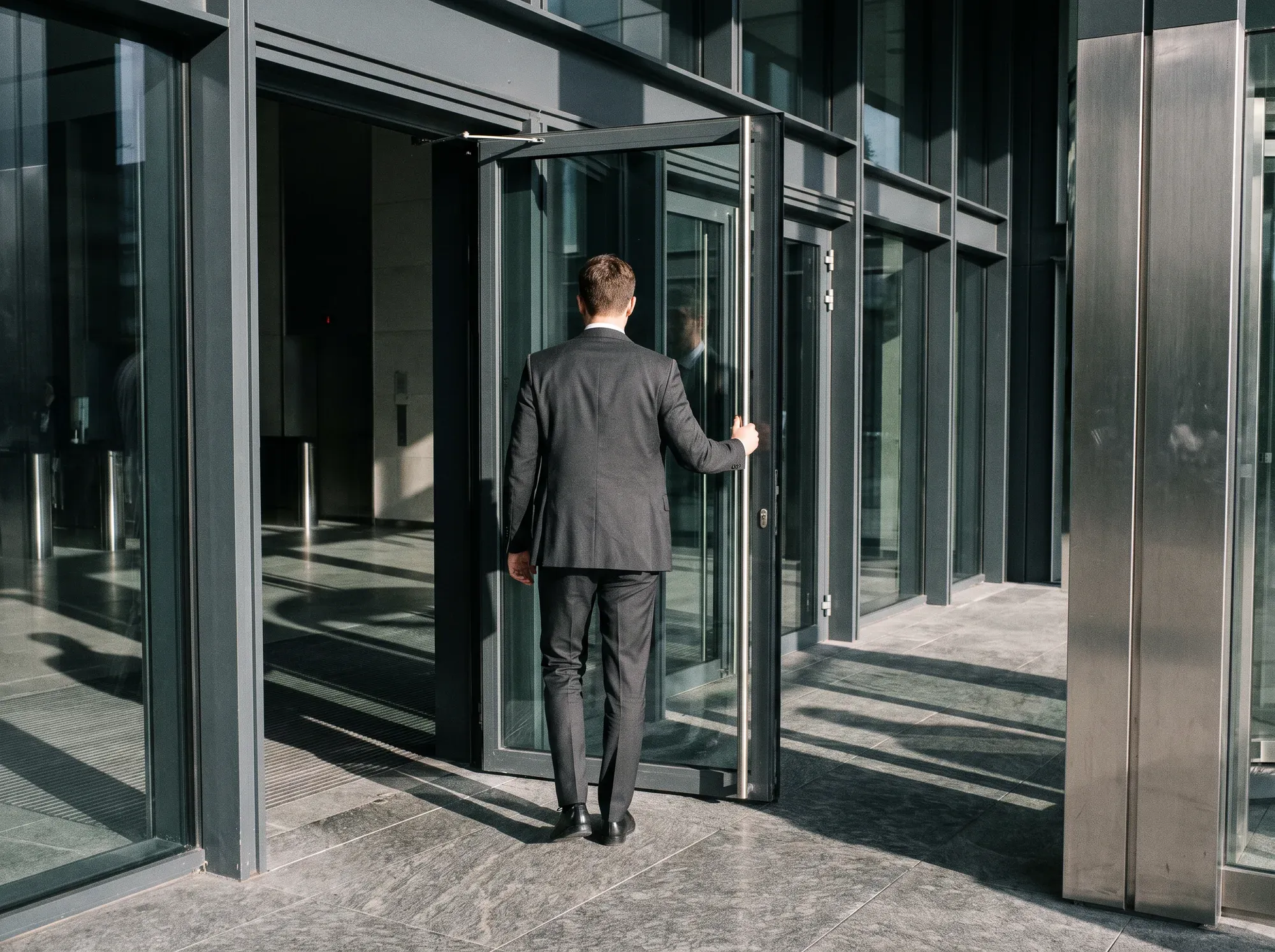 Jeune professionnel vu de dos qui entre dans un immeuble de bureaux en verre.